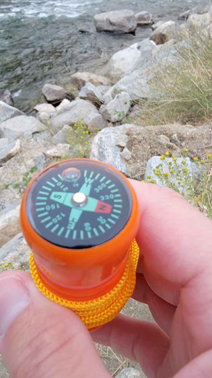 Compass feature of an orange 5-in-1 survival whistle shown in hand, useful for orientation during camping, hiking, or emergency scenarios.