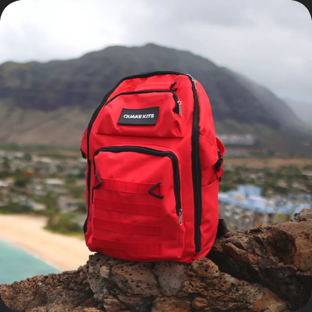 Earthquake survival kit on rock overlooking town. Kit for backpacking, hiking, overlanding. Showing hurricane and tsunami evacuation utility. Survival Kit with NOAA radio inside. 