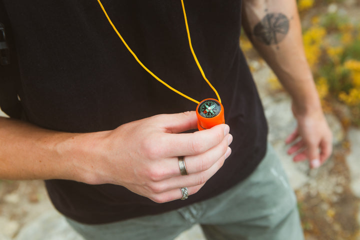 Orange survival whistle with compass held by a person, highlighting its compact size and usability for emergency navigation and signaling
